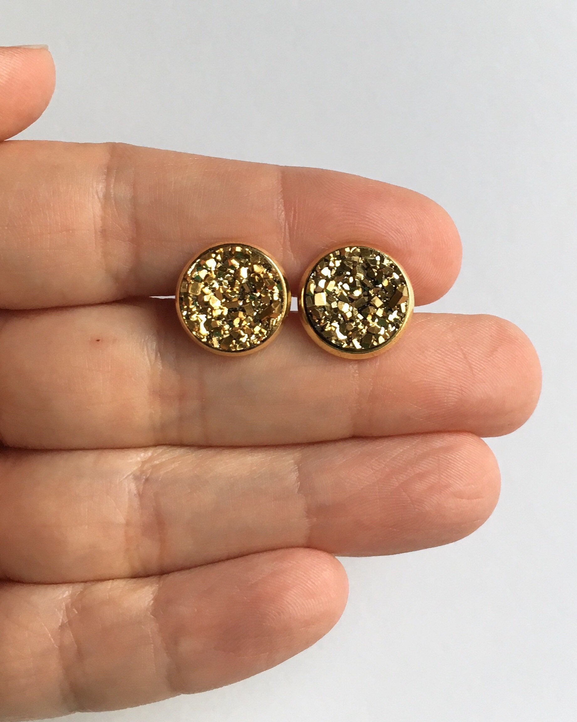 Hand holding Gold resin druzy stone stud earrings is set in a yellow gold color setting between fingers
