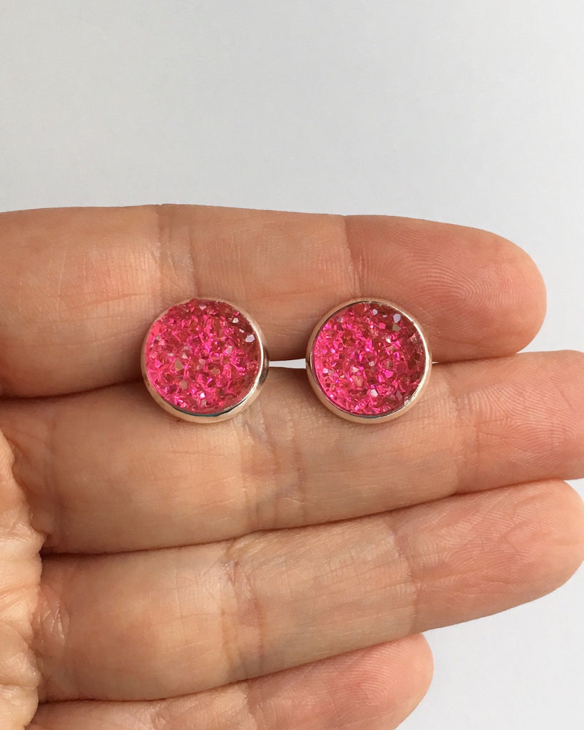 Hand holding Flamingo Pink Druzy stone Stud Earrings in a silver setting between fingers.