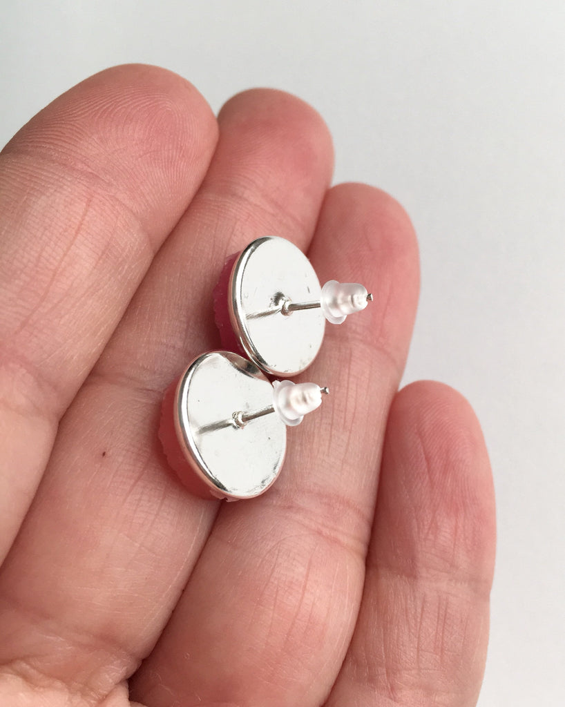 Hand holding stud earrings show silver backs with rubber push backs.