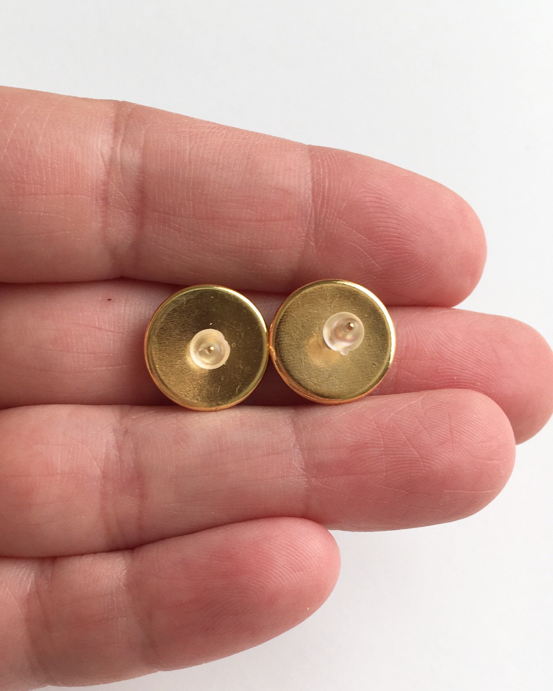 Hand holding gold stud earrings with rubber push backs.