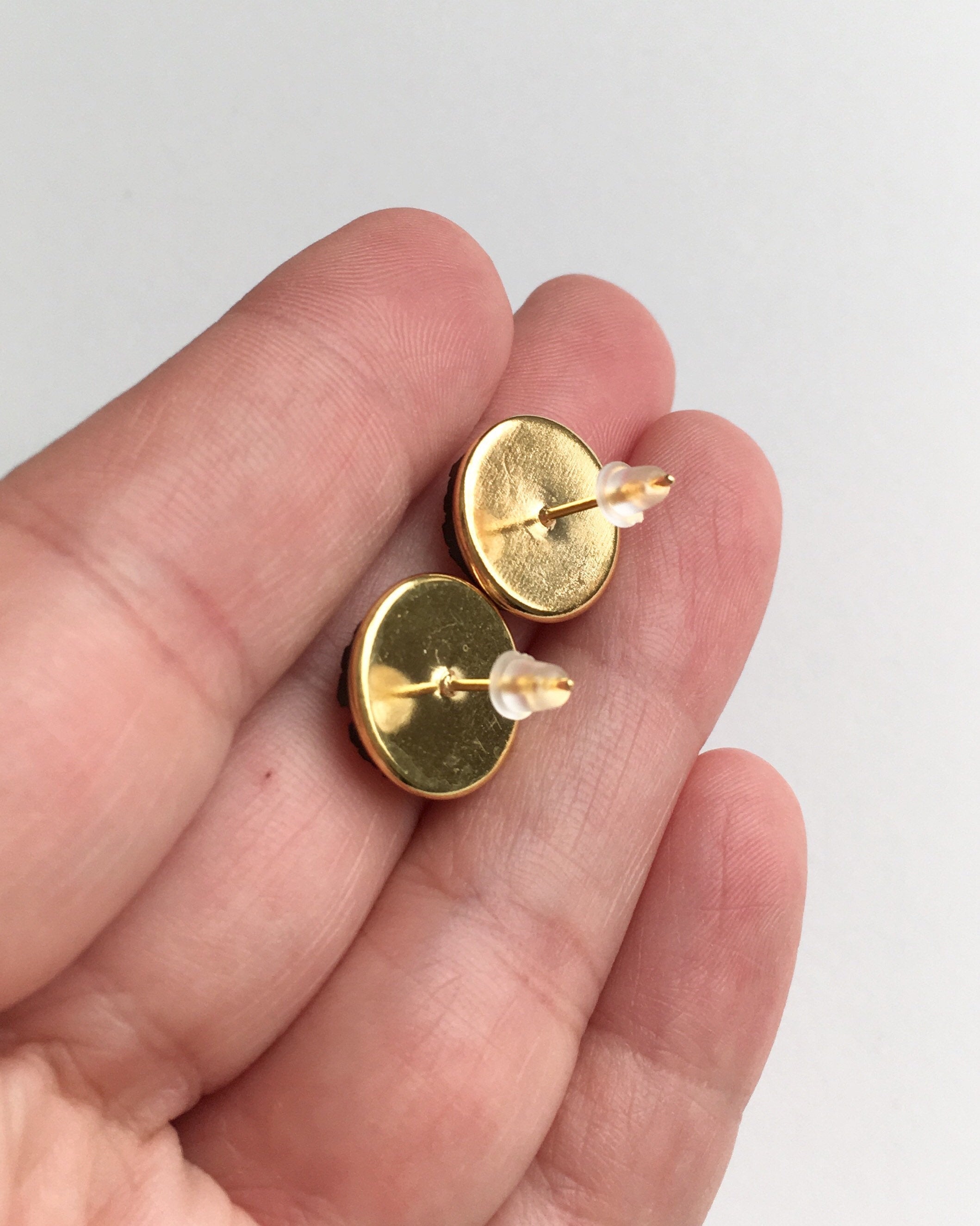 Hand holding gold setting stud earrings with rubber push back.