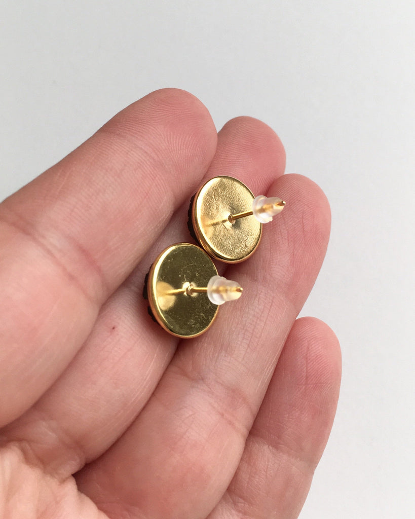 Hand holding gold setting stud earrings with rubber push back.