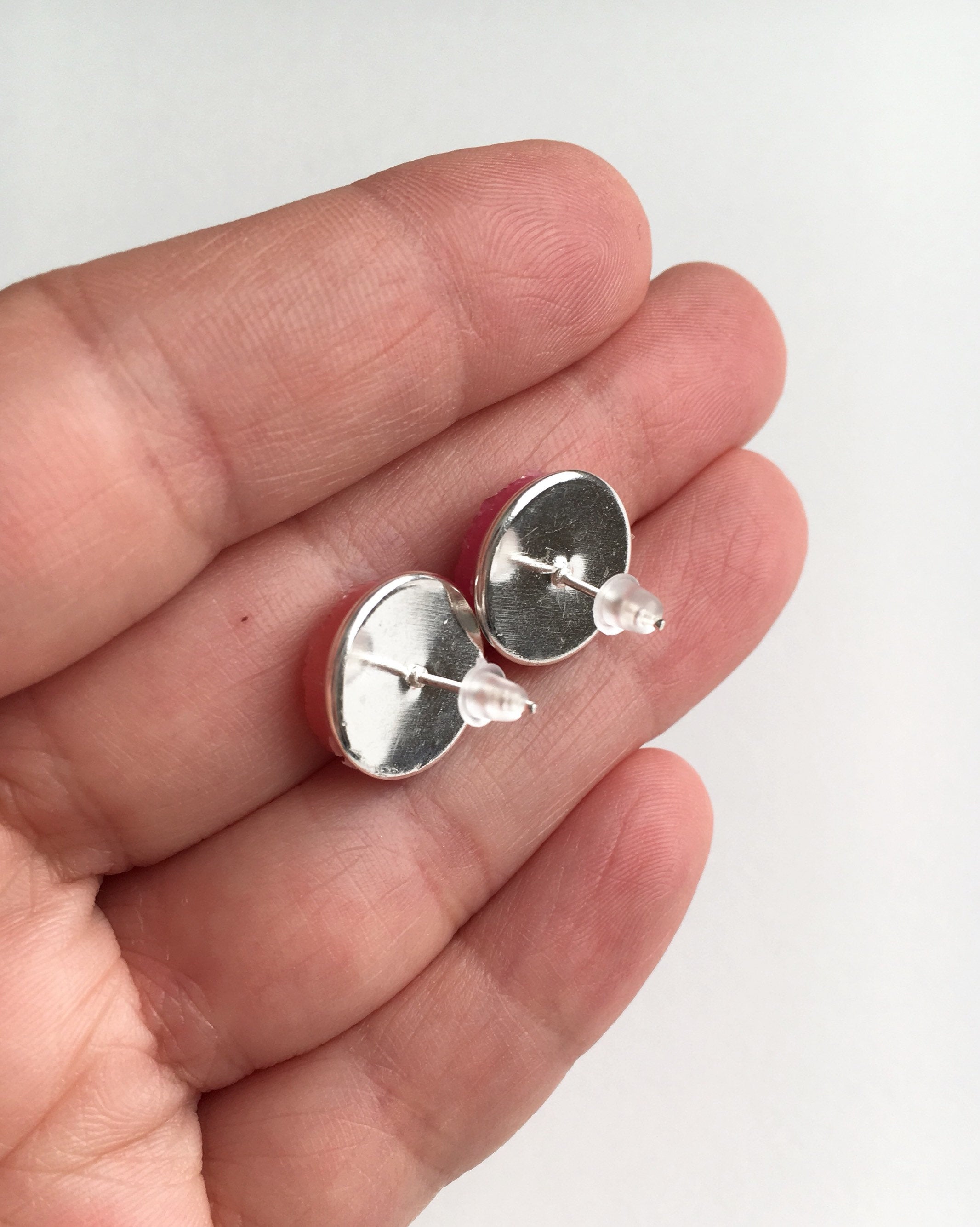 Hand holding stud earrings showing the back with rubber push backs.