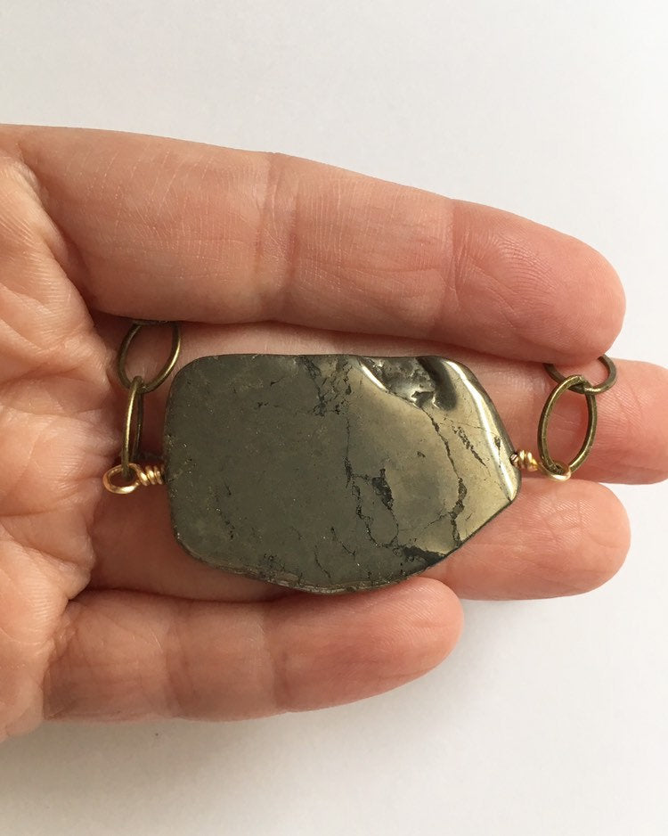 Hand holding stone of Sliced pyrite stone hand wired onto yellow gold antique brass plated chain necklace.