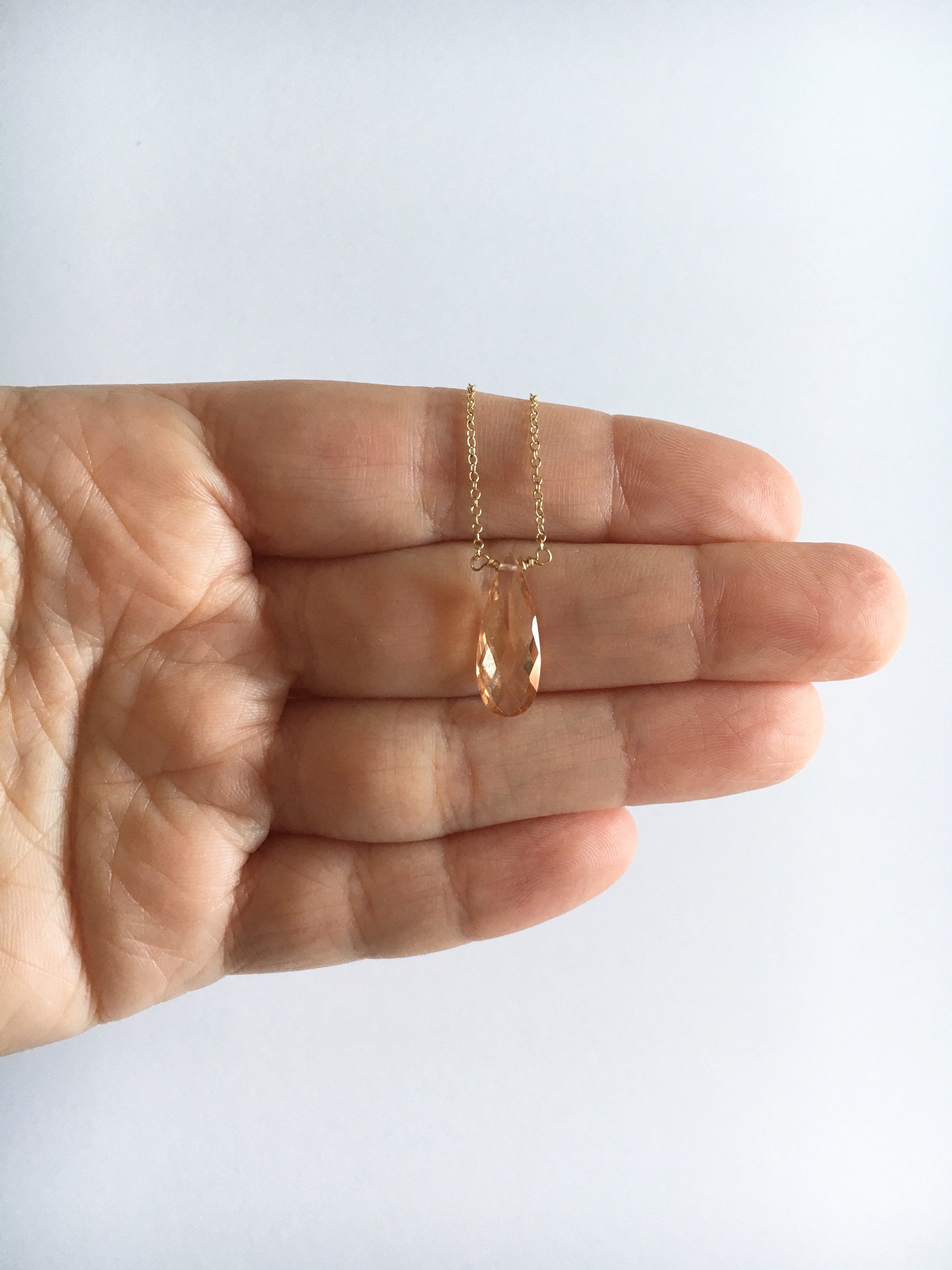Cubic zirconia teardrop crystal pendant on gold filled chain necklace – available in champaign laying over fingers.