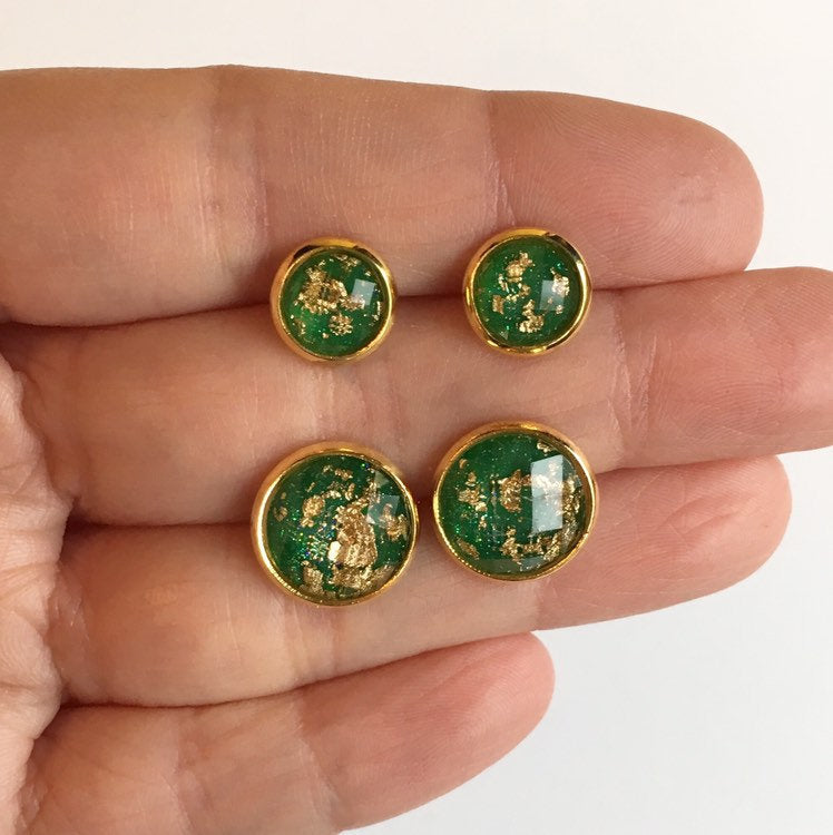 hand holding Emerald green with gold leaf resin stone stud earrings in yellow gold color setting between fingers