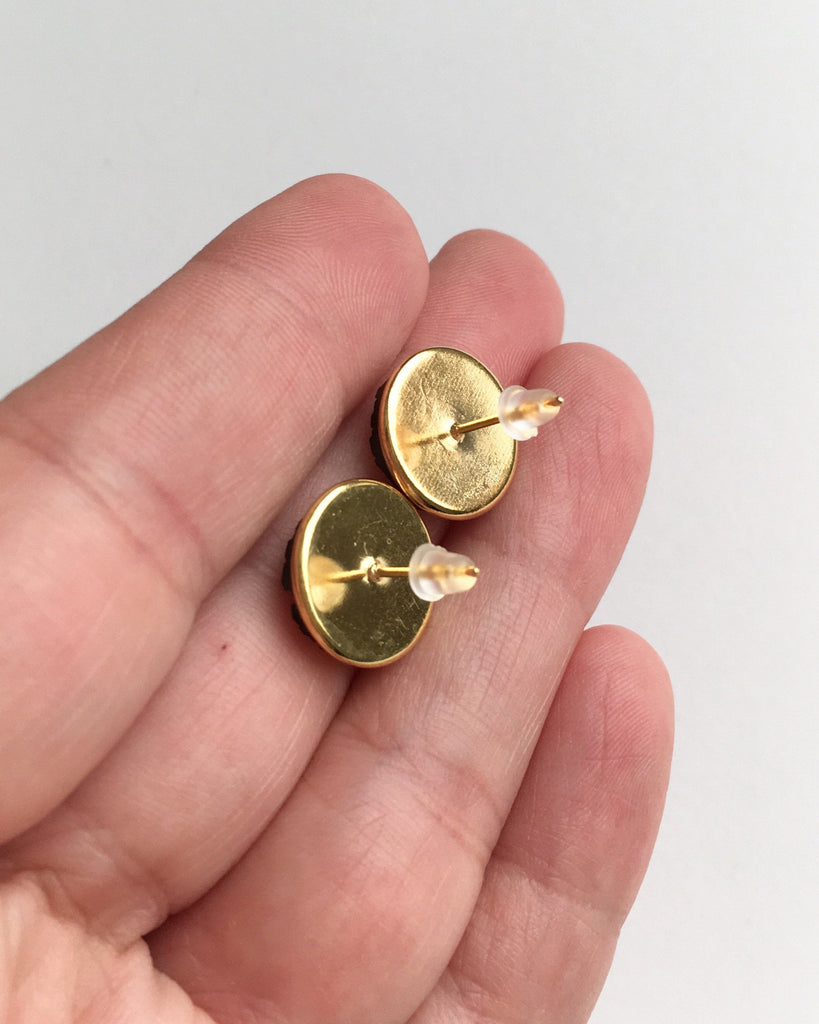 Hand holding earrings showing the yellow gold  setting back with rubber push backs.