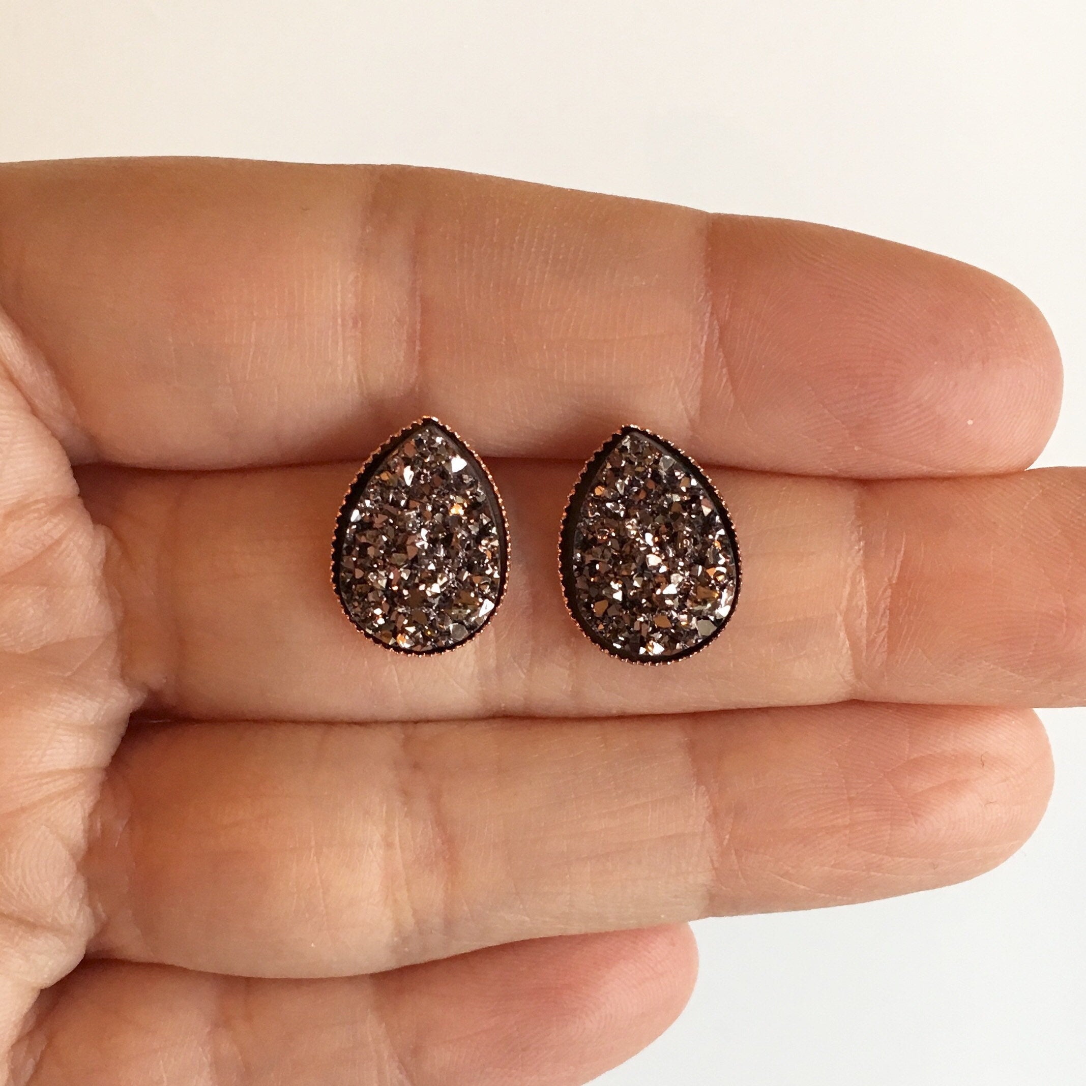 Hand holding Rose gold teardrop resin druzy stone stud earrings set in a rose gold color setting. 