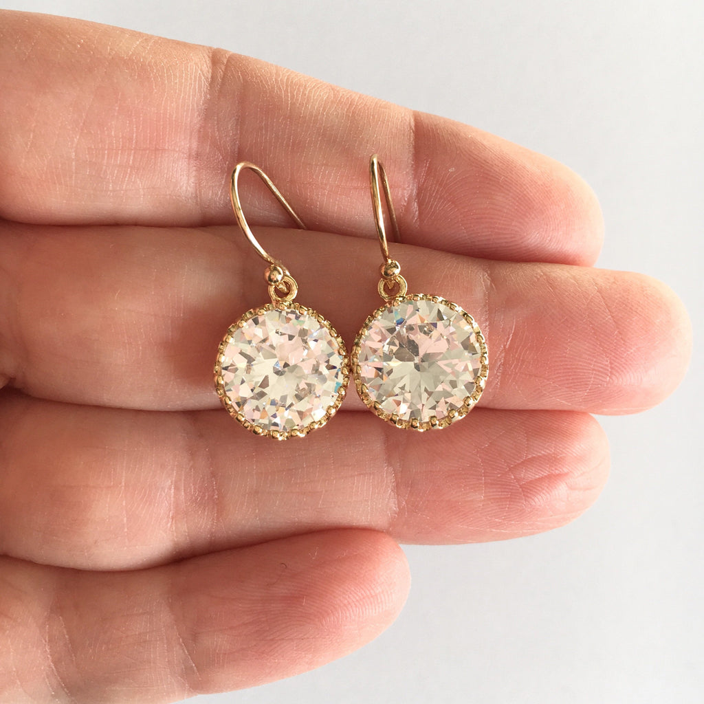 Hand holding Round cubic zirconia stone earrings set in a gold plated brass setting. 