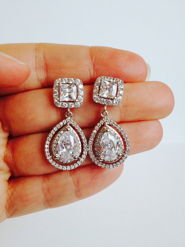 Hand holding Cubic zirconia teardrop crystal earrings in a silver colored rhodium plated brass setting. 