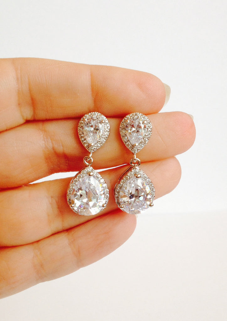 Hand holding Cubic zirconia teardrop crystal earrings in a silver colored rhodium plated brass setting.