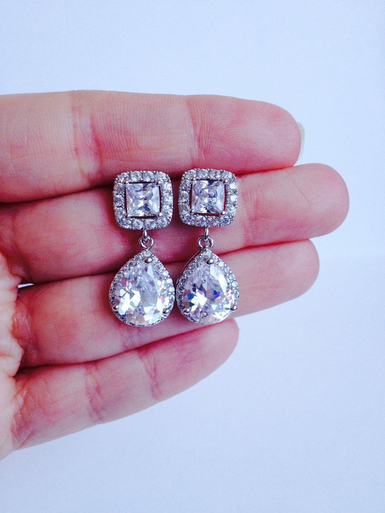 Hand holding Cubic zirconia teardrop crystals earrings in a silver colored rhodium plated brass setting.