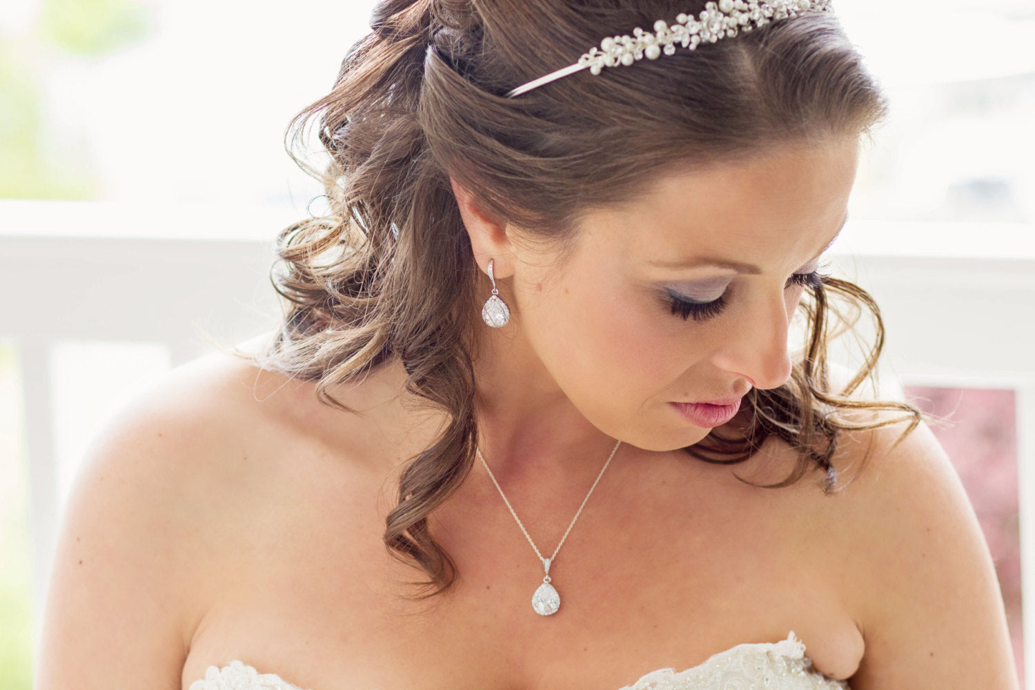 Bride wearing Teardrop cut cubic zirconia crystals set in silver color rhodium plated brass pendant necklace and earrings.