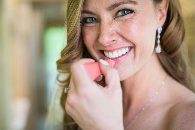 Bride applying lip gloss and wearing Long Clear cubic zirconia teardrop crystal earrings in a silver colored rhodium plated brass setting.
