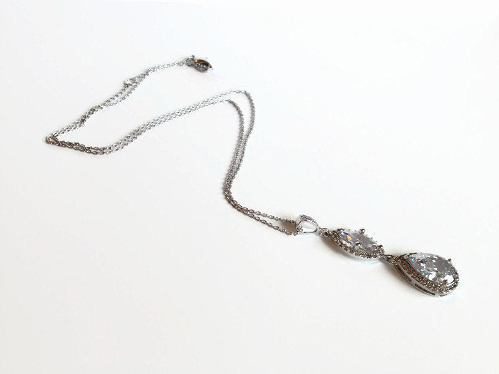 Cubic zirconia crystals set in silver color rhodium plated brass pendant necklace laying on table.