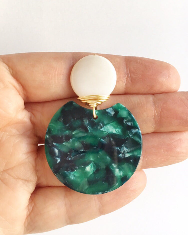 Hand holding one Mother of Pearl, Green Lucite, and Gold Wire Wrapped Earrings across her fingers.