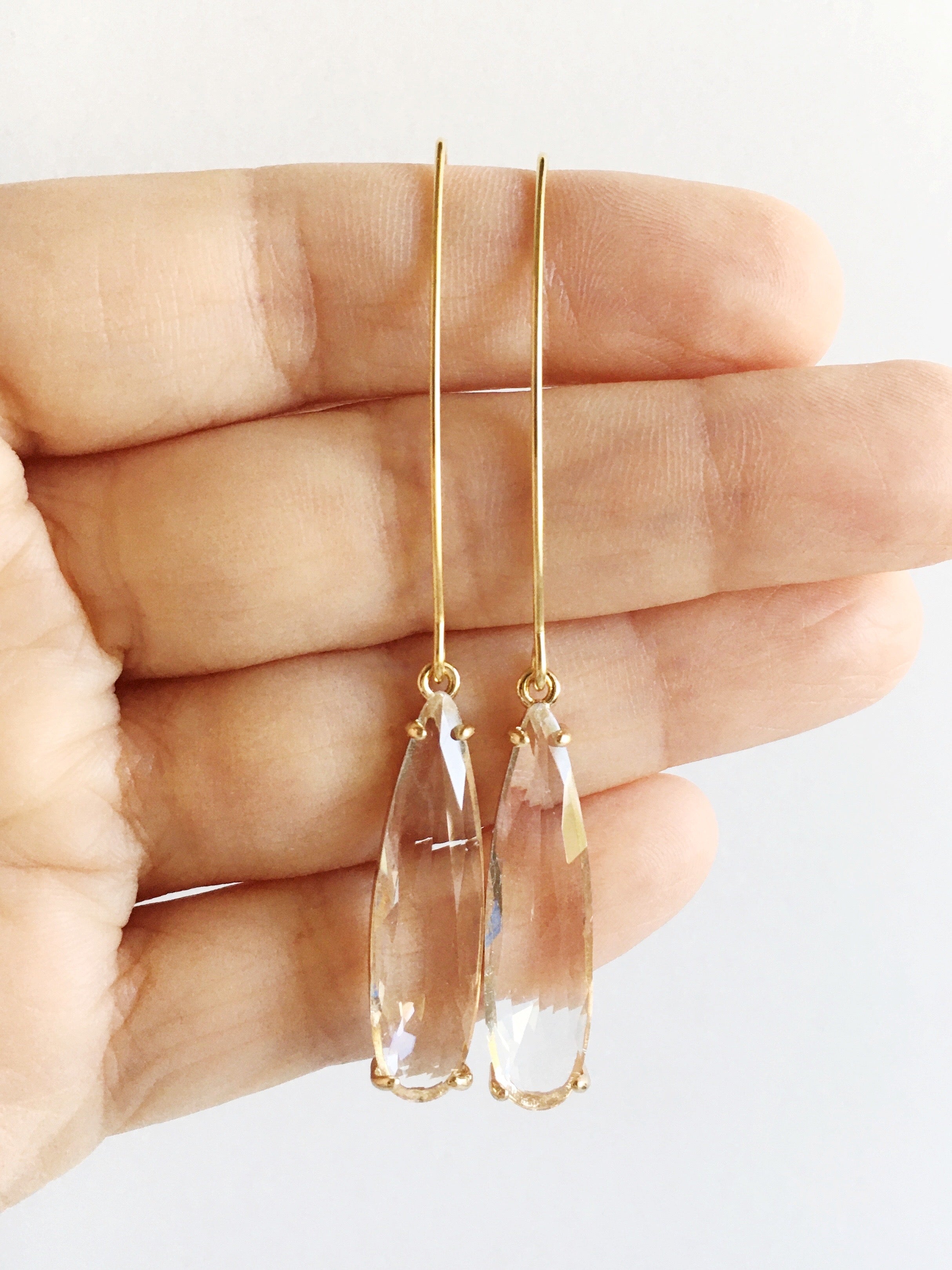 Crystal clear Glass Teardrop and Gold Long Dangle Earrings hanging from women's fingers
