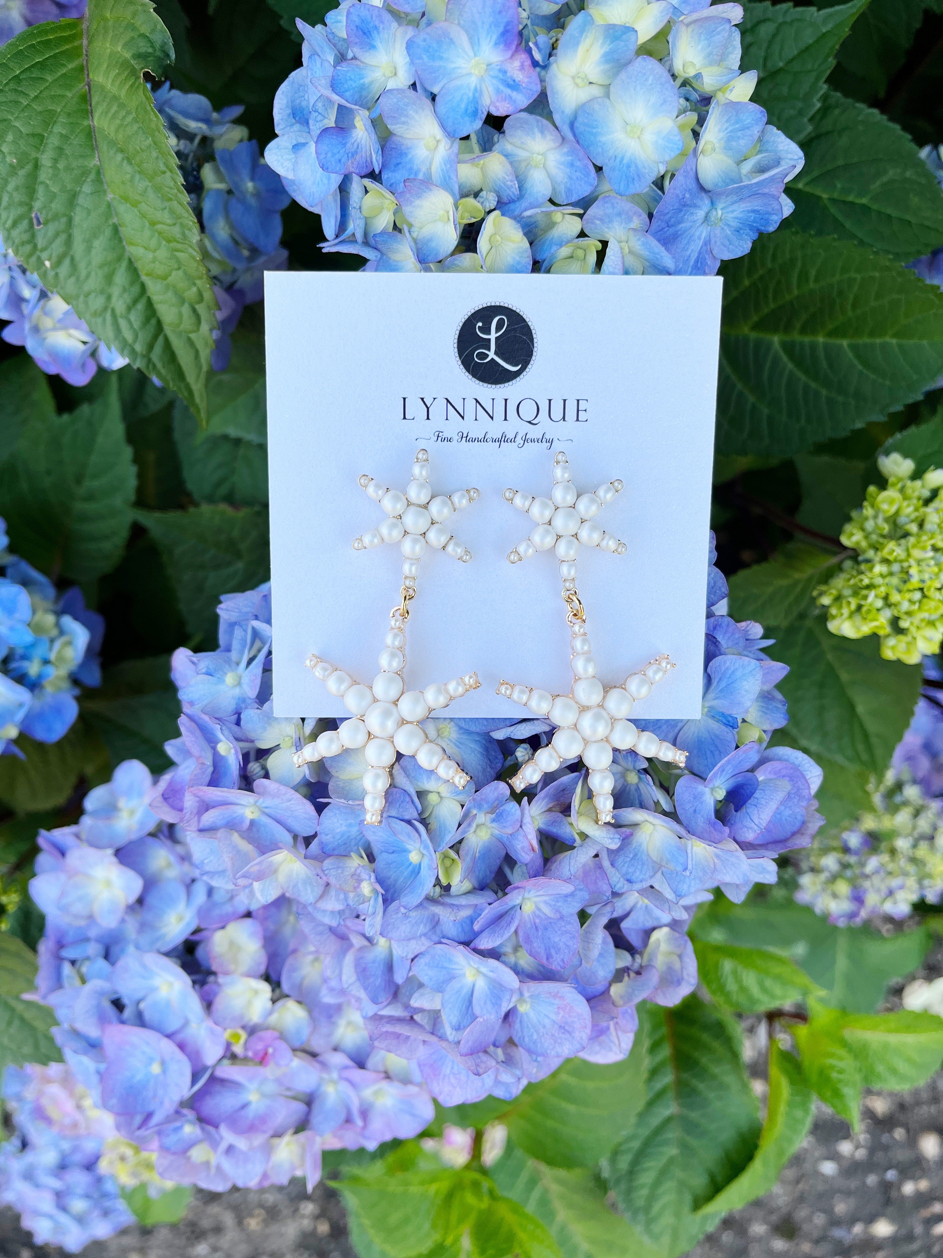 star pearl and yellow gold statement earrings displayed on blue hydrangea plant