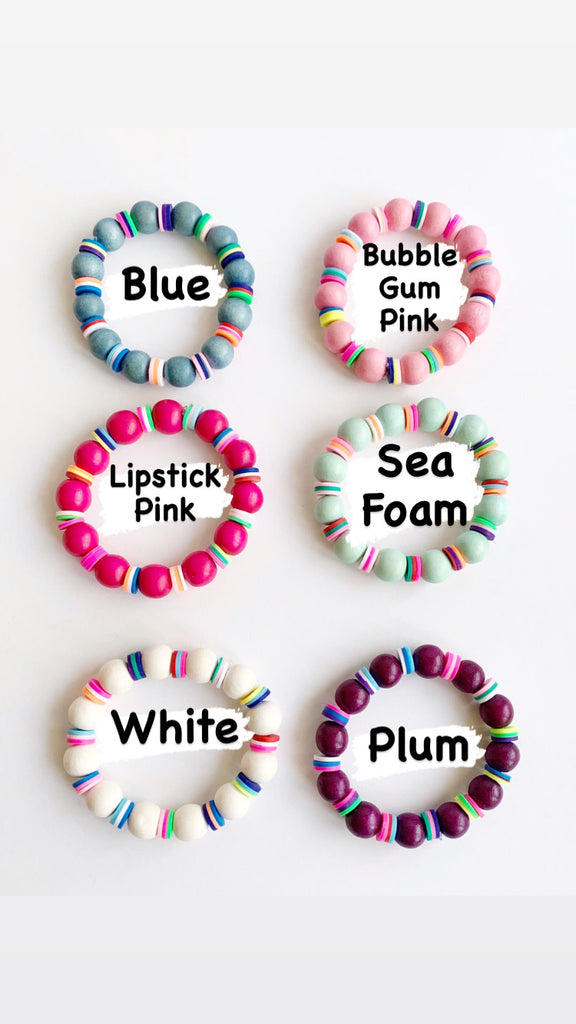 Children's White and Rainbow Confetti Stretch Bracelets in Blue, Bubble Gum Pink, Lipstick Pink, Sea Foam, White, and Plum on table.