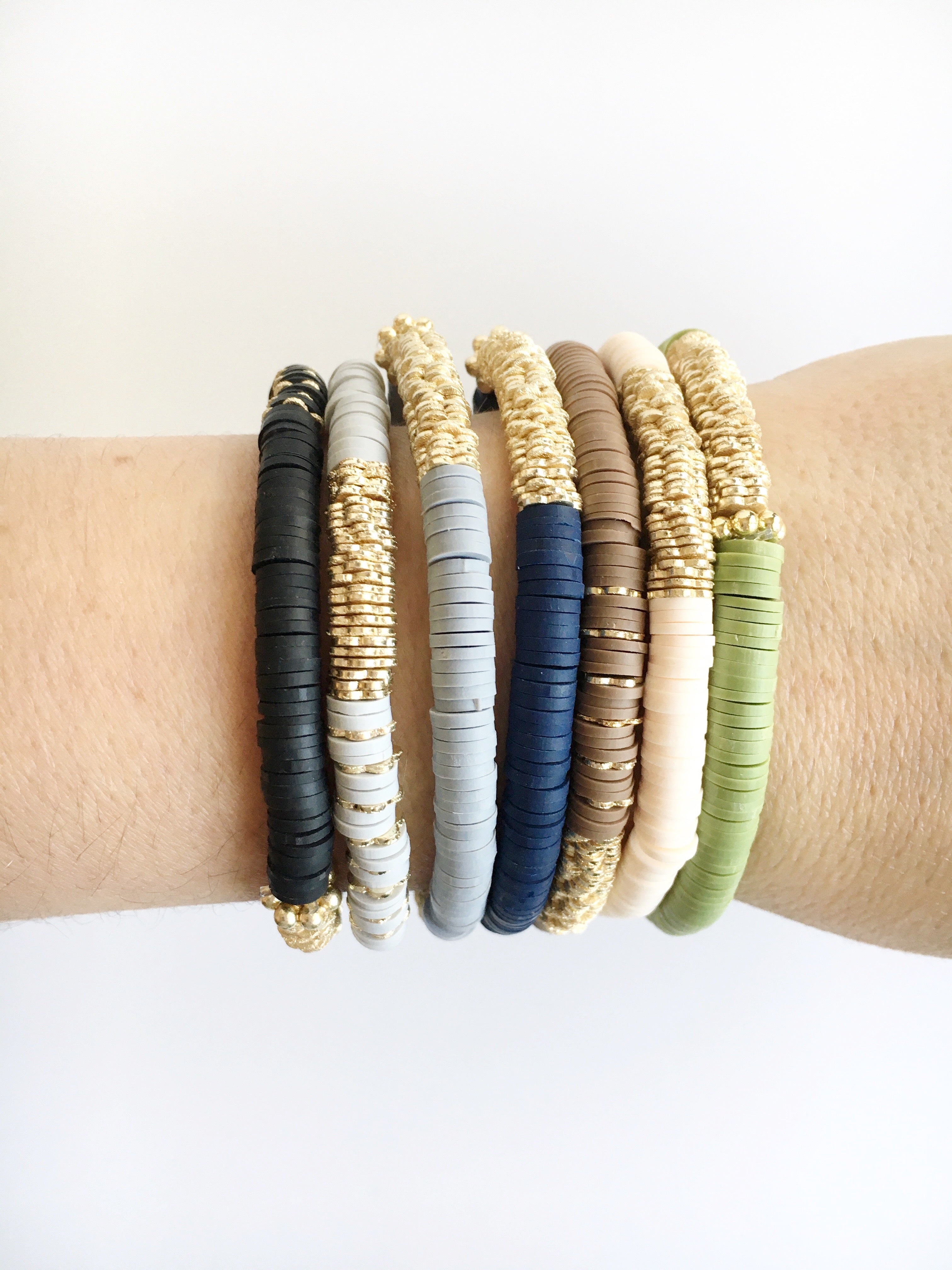 Women's wrist wearing Top view of stretch beaded bracelets in Black, Light gray, dark gray, navy blue, brown, vanilla, and olive.