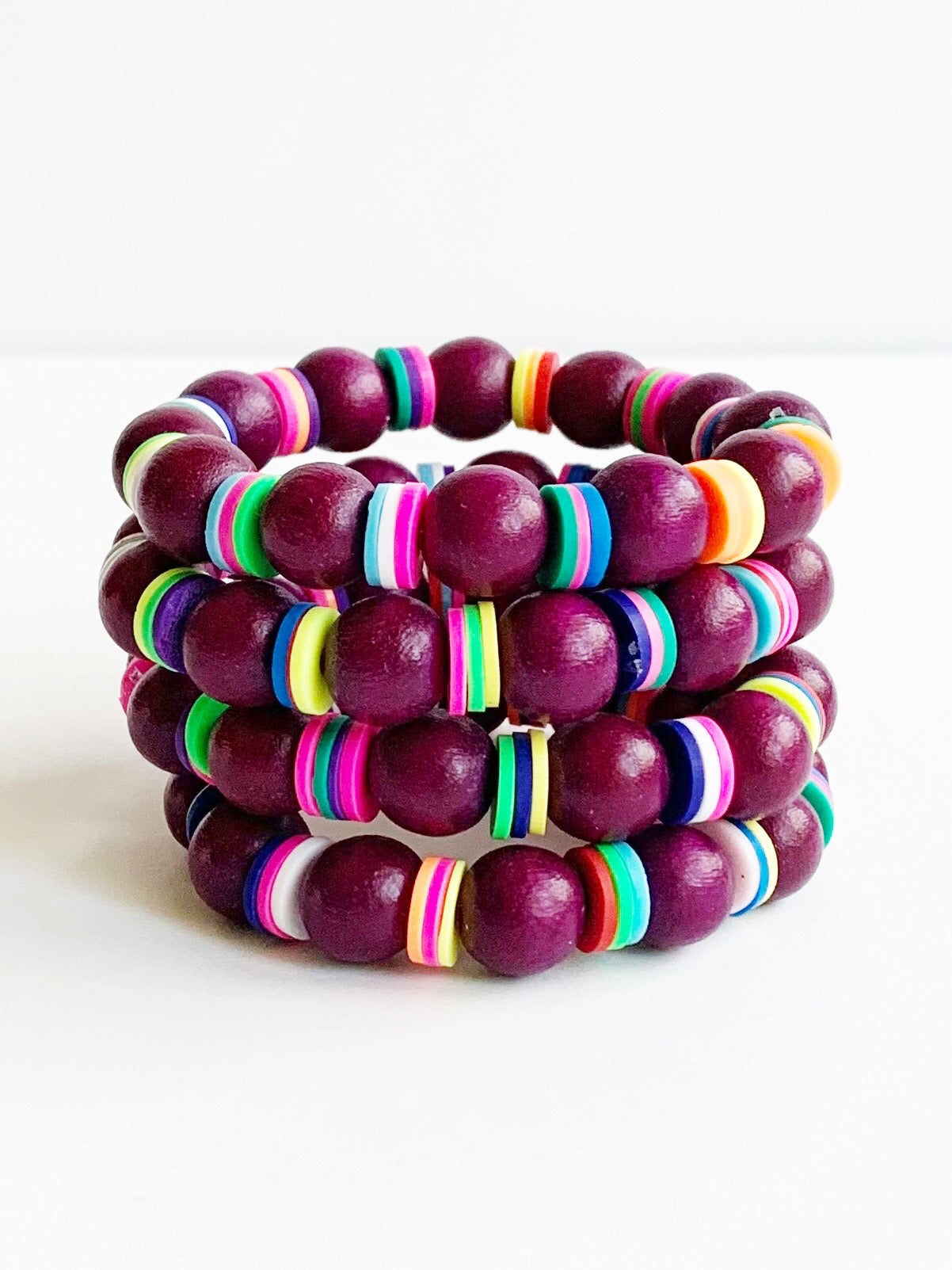 Four Child sized Plum and rainbow confetti beaded stretch bracelets stacked.