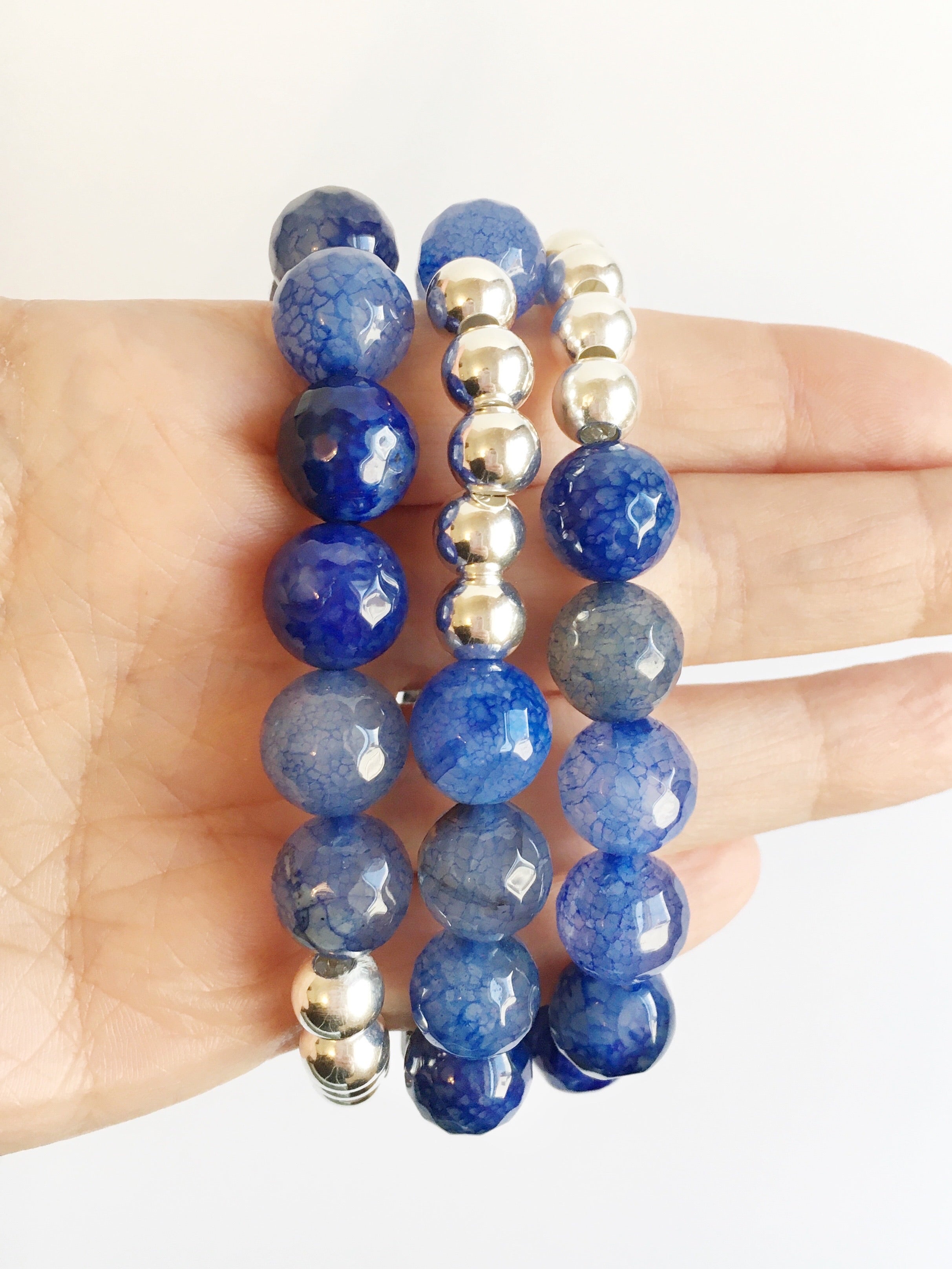 Hand holding Blue Striped Agate and Silver Beaded Stretch Bracelets on fingers.