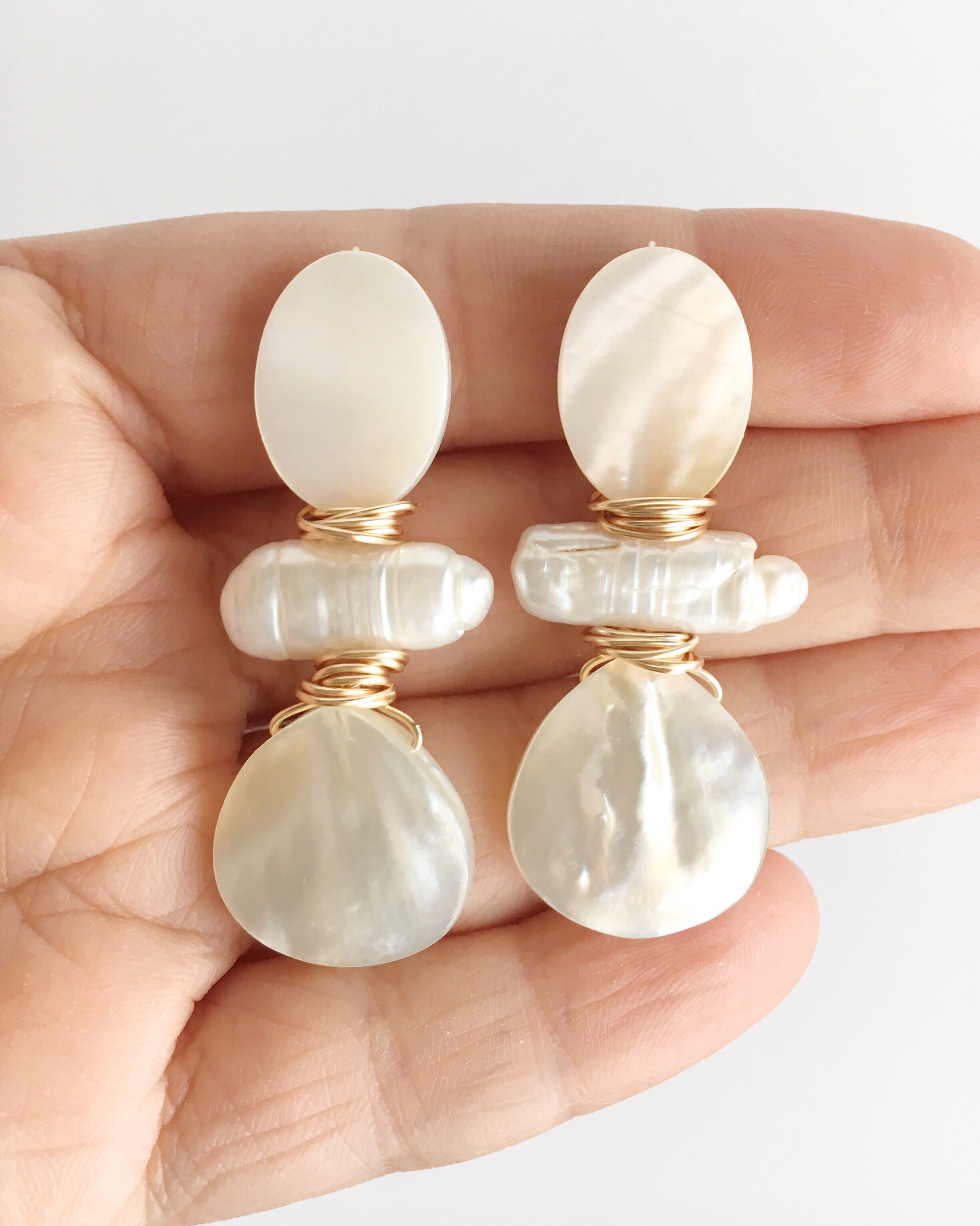 Hand holding Three Stone Mother of Pearl and pearl stone earrings wrapped with gold plated wire