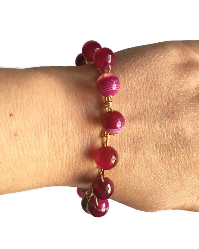 Women's wrist wearing pink agate gemstone and gold bangle bracelet. 