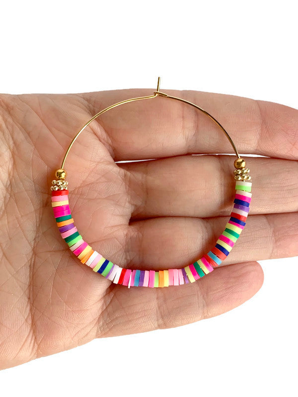 Hand holding Rainbow heishi beads on gold colored hoop earrings