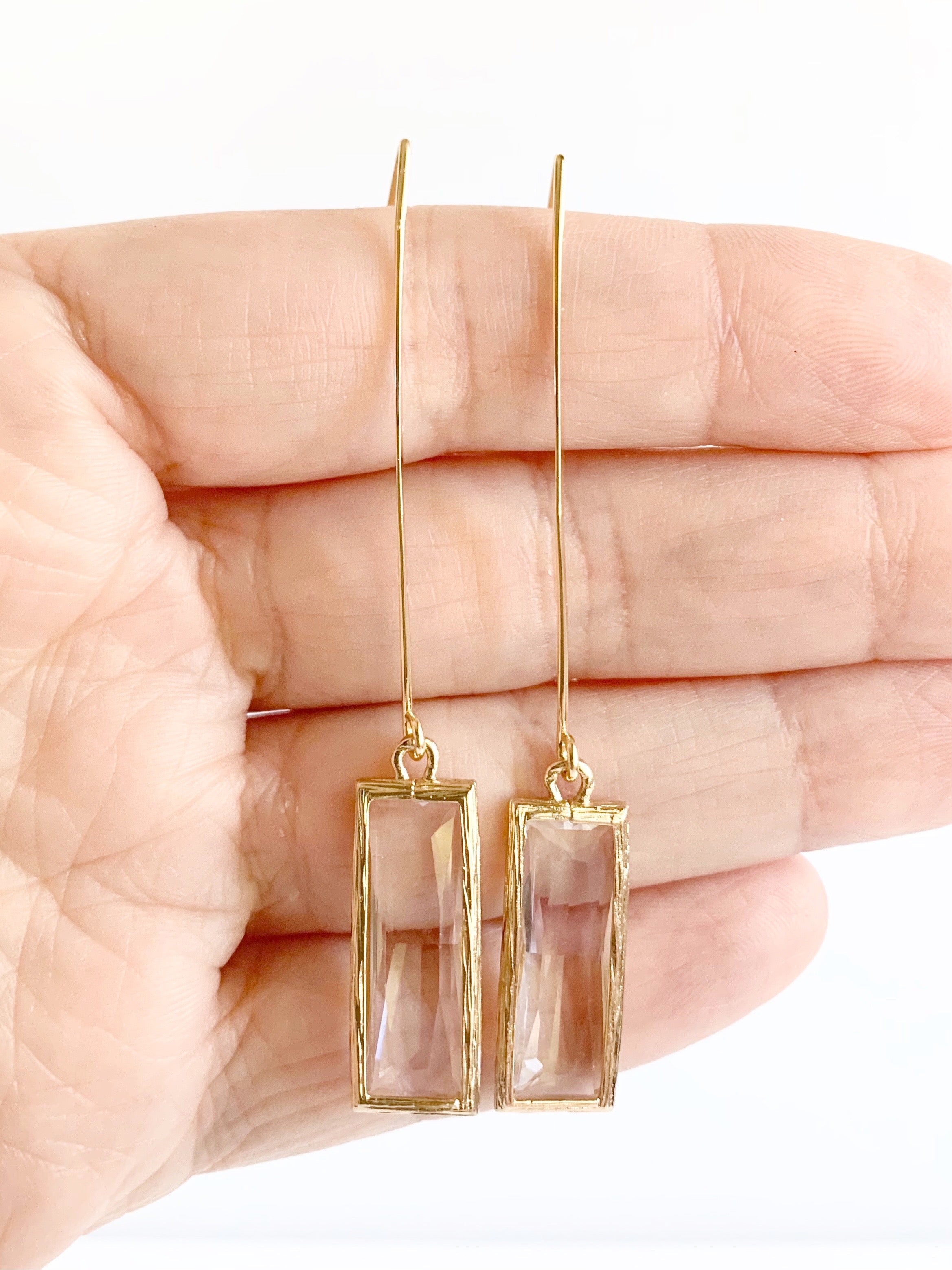 long gold pendant earrings displayed on hand
