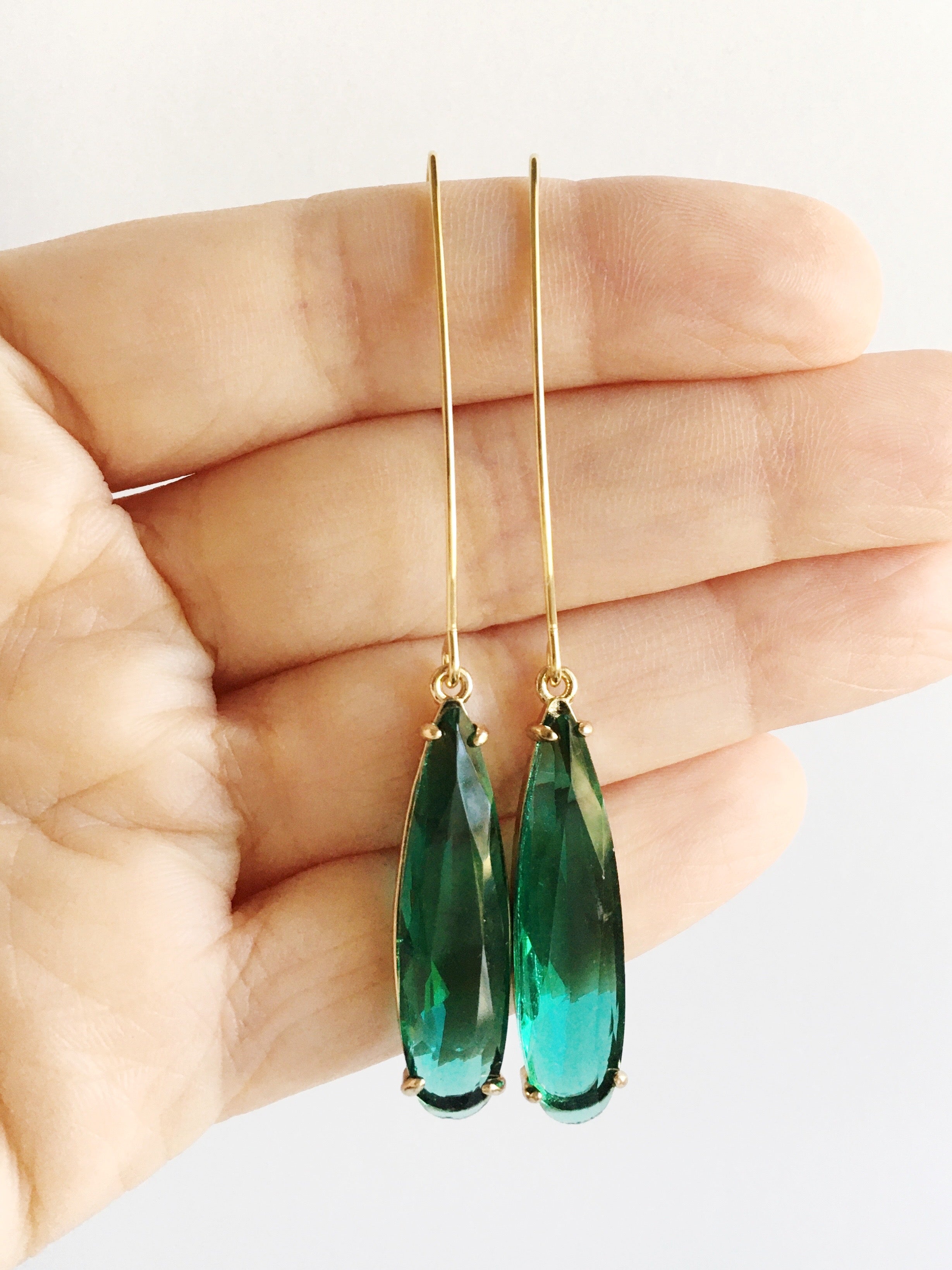 emerald green pendant earrings displayed on hand