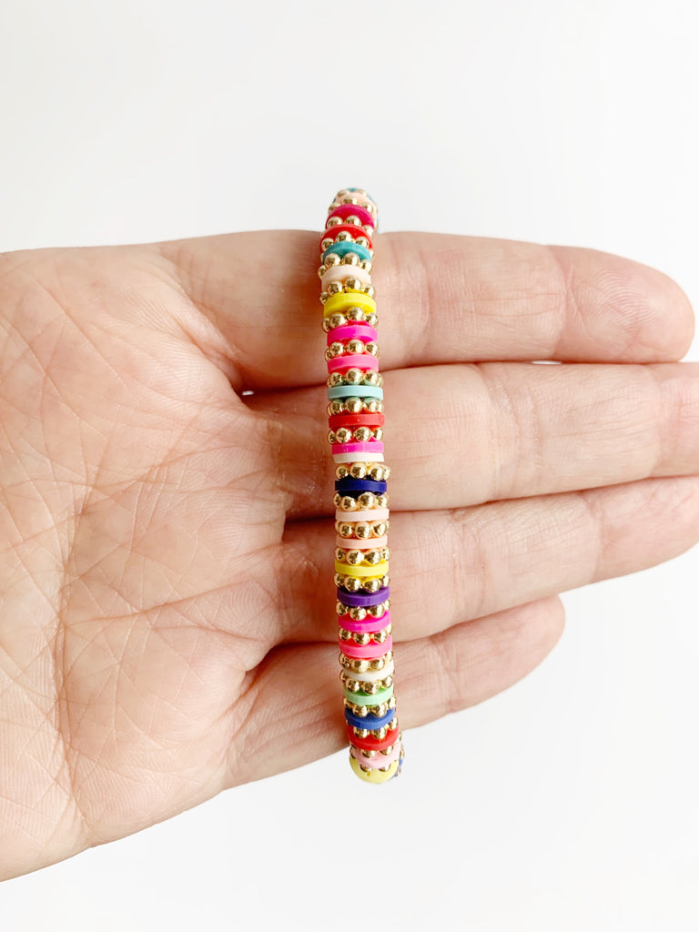 Hand holding  Gold and Rainbow Confetti Stretch Bracelet over fingers.