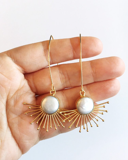 Gold sunburst and pearl statement earrings held in hand