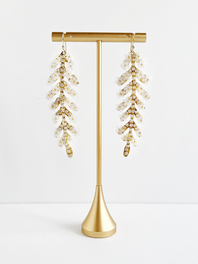leaf shaped gold statement earrings with crystals and white flowers displayed on gold t stand