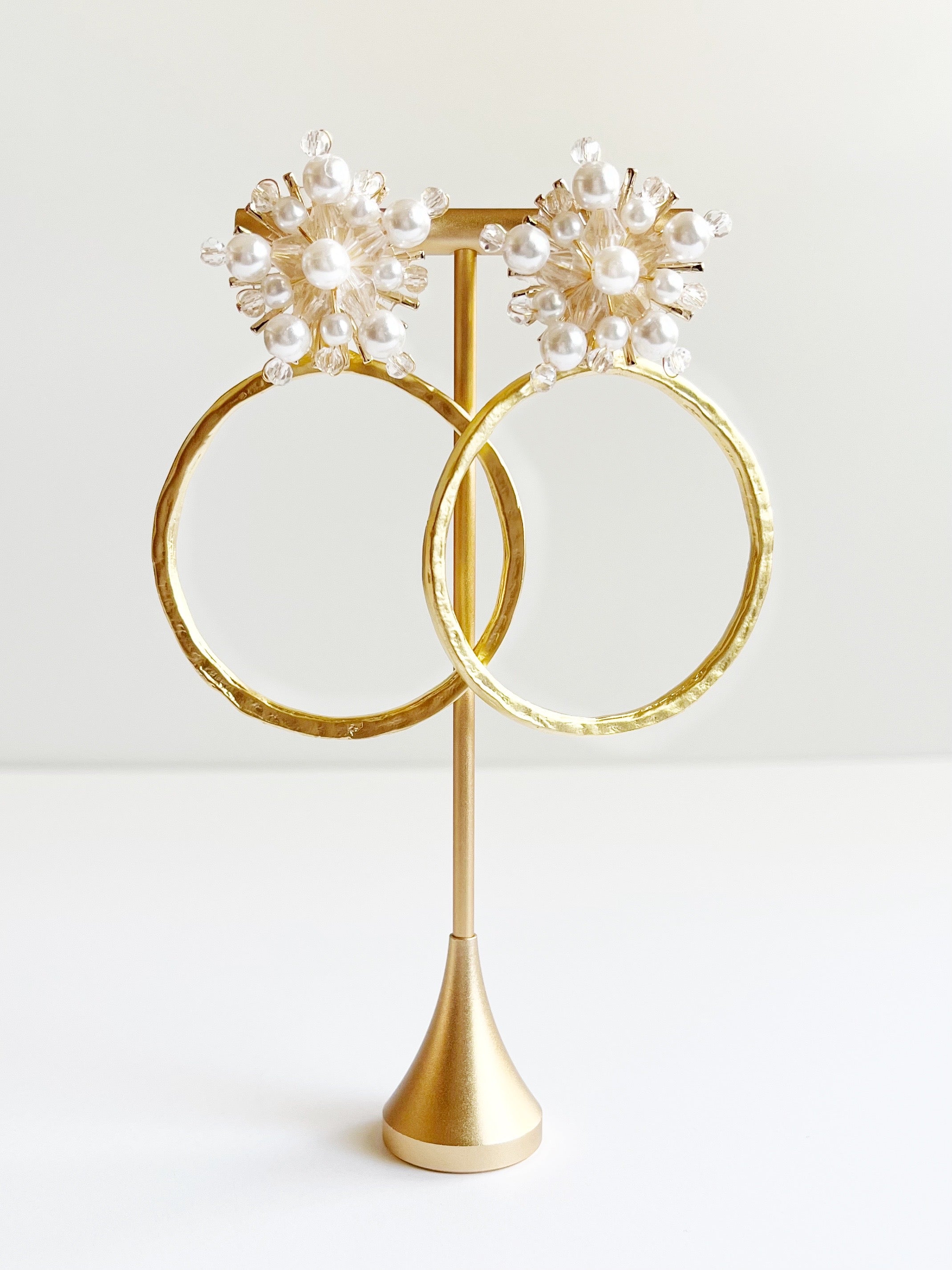 yellow gold hoop statement earrings with crystal and pearl stud displayed on gold earring t stand